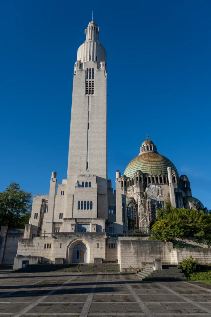 The Inter-Allied Memorial tower and the green-domed Sacred Heart Church on Cointe hill in Liège, under a deep blue sky.