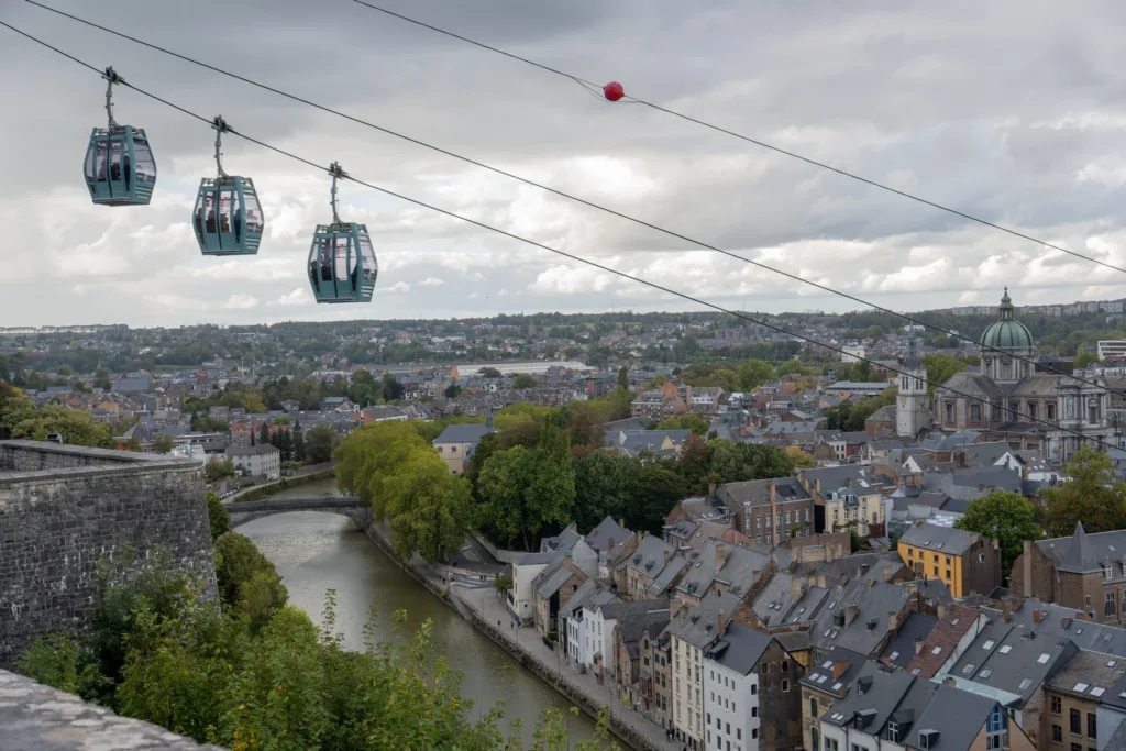 Three cabins of the Namur cable car glide over the Meuse between the old town and the citadel, under a grey autumn sky.